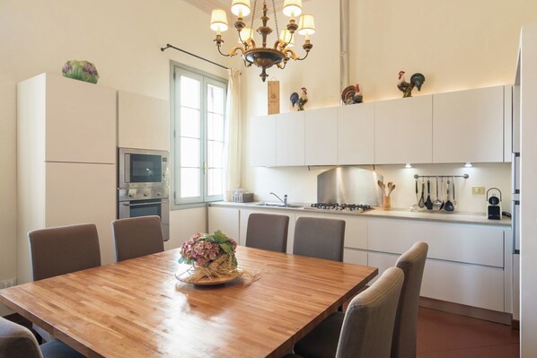Eine moderne Küche mit weißen Schränken, einem eingebauten Backofen und einem Essbereich mit Holztisch und Stühlen.