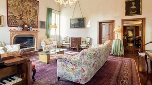 Amplia sala de estar con piano, sofás, chimenea y una araña.