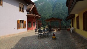 A courtyard with a wooden pergola, outdoor seating, and a mountain backdrop.