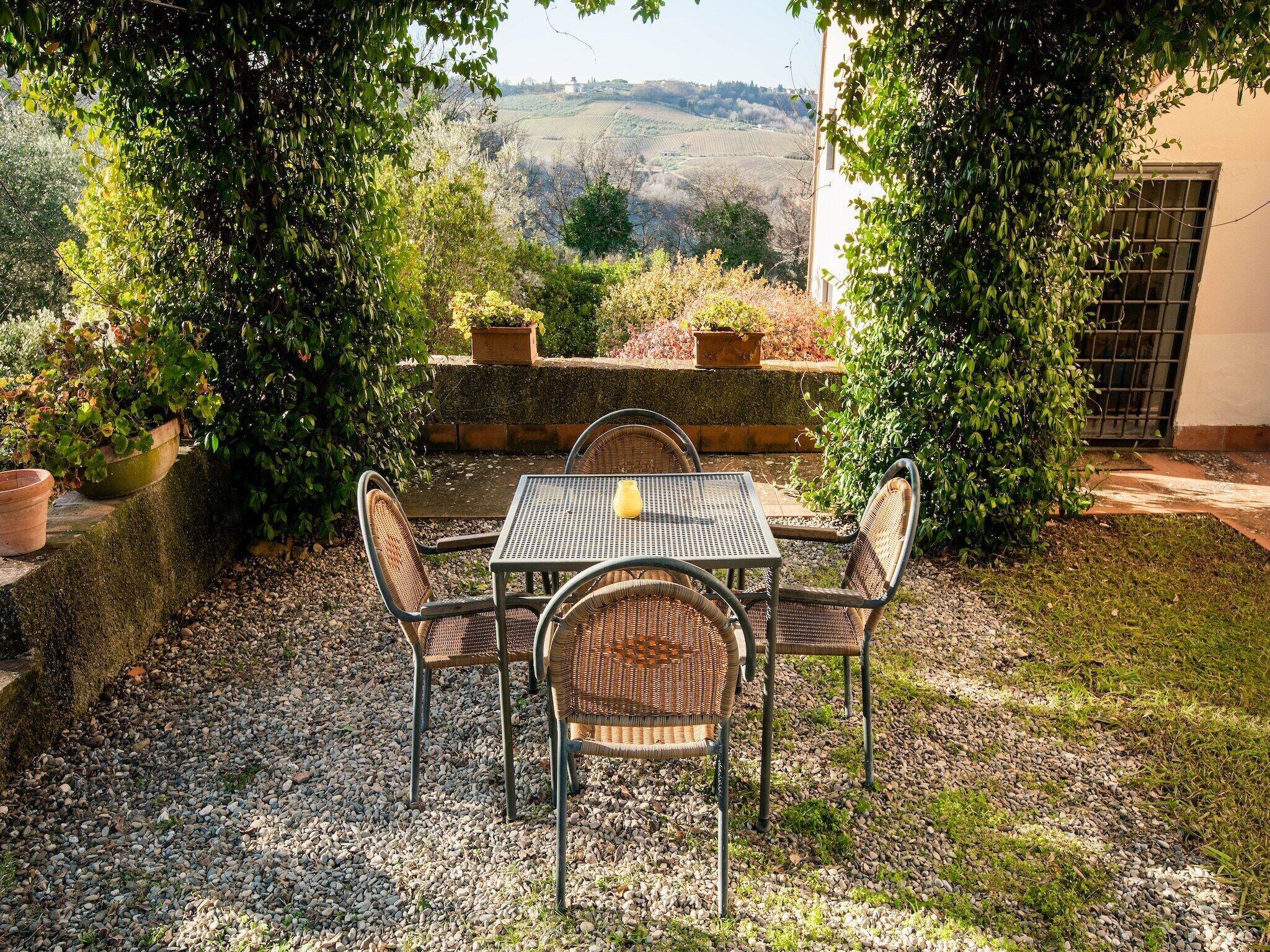 A patio with a table and chairs, surrounded by greenery and a view of rolling hills.