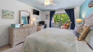 A bedroom with a bed, dresser, TV, and a balcony with curtains.