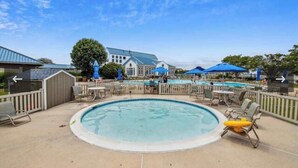 A pool area with a circular pool, lounge chairs, and umbrellas.