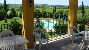 A terrace with a pool, yellow pillars, white plastic chairs, and a view of a green landscape. - Holiday Home in Tuscany with Pool & Garden (Vinci)