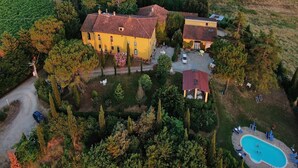 An aerial view of a property with a large yellow building, a smaller attached structure, and a swimming pool surrounded by lounge chairs. - Holiday Home in Tuscany with Pool & Garden (Vinci)