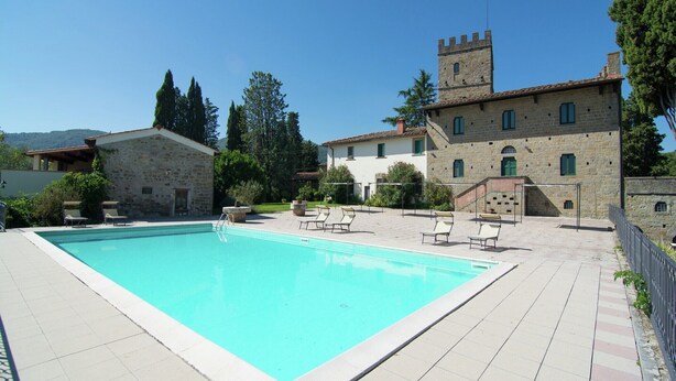 Ein Swimmingpool mit Liegestühlen, Steingebäude und einem Turm.