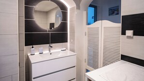 A modern bathroom with a large mirror, white vanity, and a shower area.