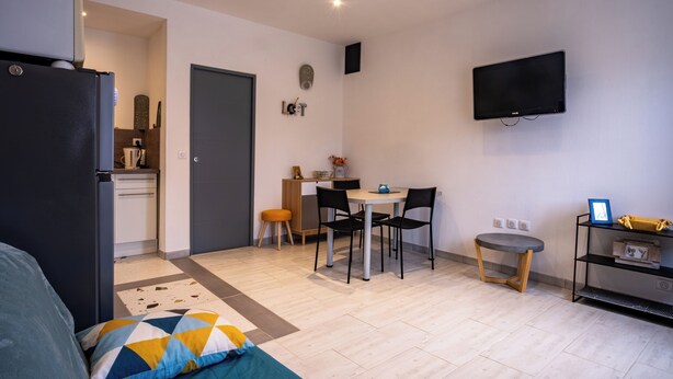 A compact living space with a kitchenette, a dining area, a TV mounted on the wall, and a small side table.