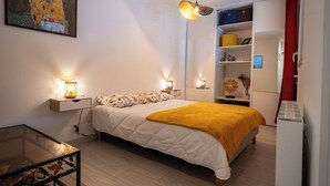 A bedroom with a bed, bedside lamps, a glass table, a painting on the wall, and a wardrobe with shelves.