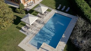 An aerial view of a swimming pool with lounge chairs and umbrellas, surrounded by a well-maintained lawn and trees.