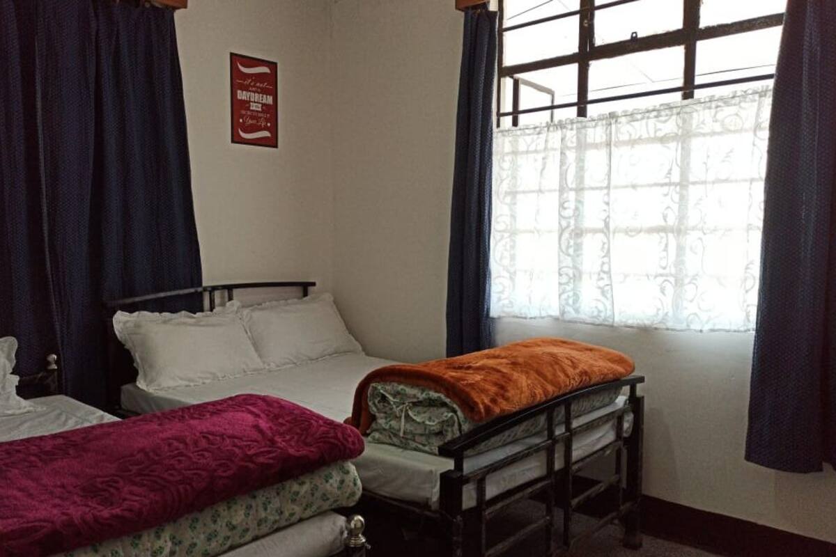 Una habitación con dos camas individuales, una con un edredón morado y la otra con uno naranja. Hay una ventana con cortina y un cartel en la pared.