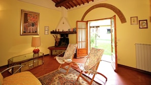 Una sala de estar acogedora con techo de madera, chimenea, sillón estampado y vista al jardín a través de un ventanal abierto.