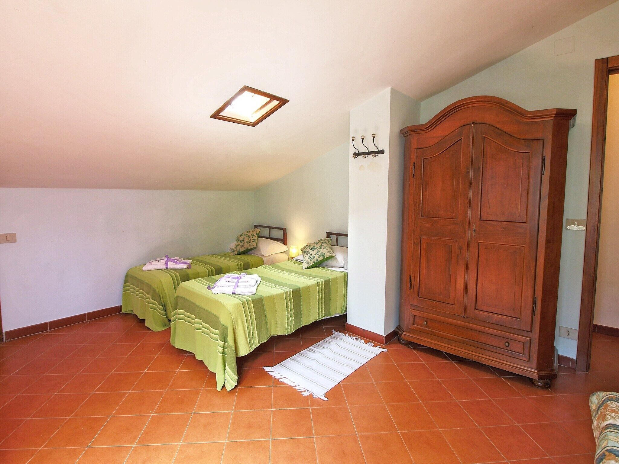 Une chambre avec deux lits, une armoire en bois et un sol carrelé.