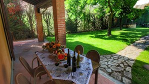 An outdoor patio with a table set for dining, surrounded by wicker chairs, and a brick pillar.