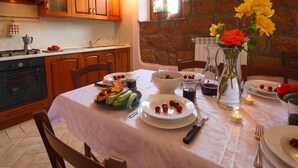 Un comedor con una mesa preparada para cuatro, una cocina al fondo y una pared de piedra.