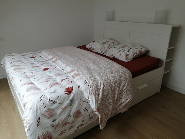 A bed with a floral bedspread and a polka dot blanket, a red pillow, and a white headboard with shelves.