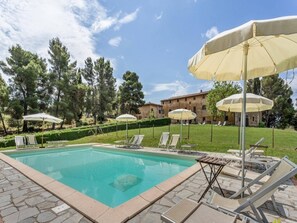 Une piscine entourée de chaises longues et de parasols, elle-même bordée d’un jardin aménagé et avec un bâtiment visible au loin.