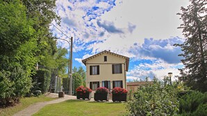 A two-story building with a garden in front, surrounded by trees and a clear sky. - Flat in Piticchio with Scenic Views & Pool (Arcevia)