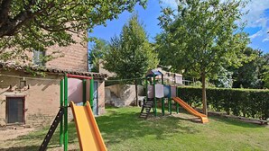 A playground with slides and climbing structures, surrounded by a grassy area and trees. - Flat in Piticchio with Scenic Views & Pool (Arcevia)
