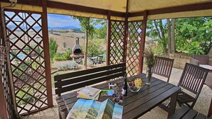 A covered patio with a wooden table, a bench, and a grill. - Flat in Piticchio with Scenic Views & Pool (Arcevia)