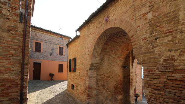 A cobblestone street with brick buildings, an archway, and a sign reading "GIRO MURA". - Flat in Piticchio with Scenic Views & Pool (Arcevia)