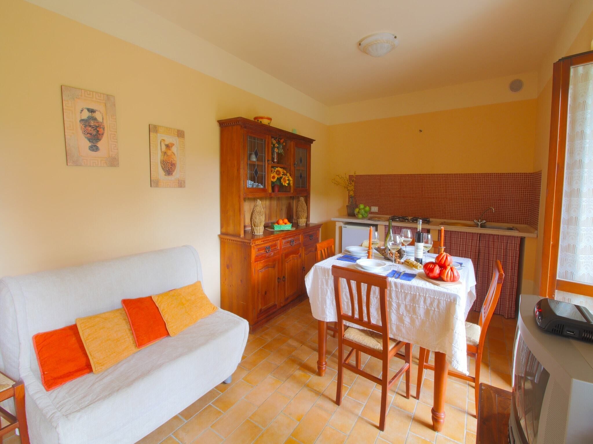 Uma sala de estar aconchegante com um sofá branco, uma mesa de jantar de madeira para dois lugares e uma cozinha com painel de azulejos e armários de madeira.