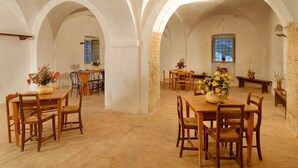 A spacious dining area with high arched ceilings and rustic brick walls. Tables and chairs are arranged for dining, with flower arrangements on the tables. - Apartment in Marche with Pool & Terrace (Apecchio)