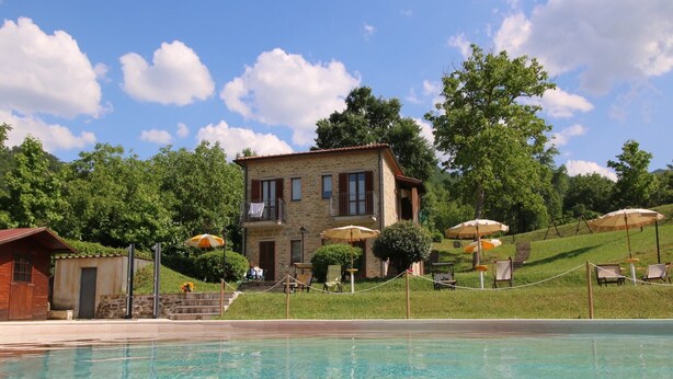 A pool area with a stone building, outdoor seating, and umbrellas. - Apartment in Marche with Pool & Terrace (Apecchio)