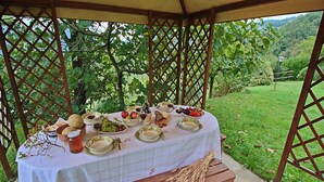 Un área de comedor al aire libre techada, con una mesa lista para una comida, rodeada de vegetación.