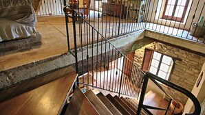 Un espacio habitable en varios niveles, con una escalera de madera, paredes de piedra y una zona de estar acogedora.