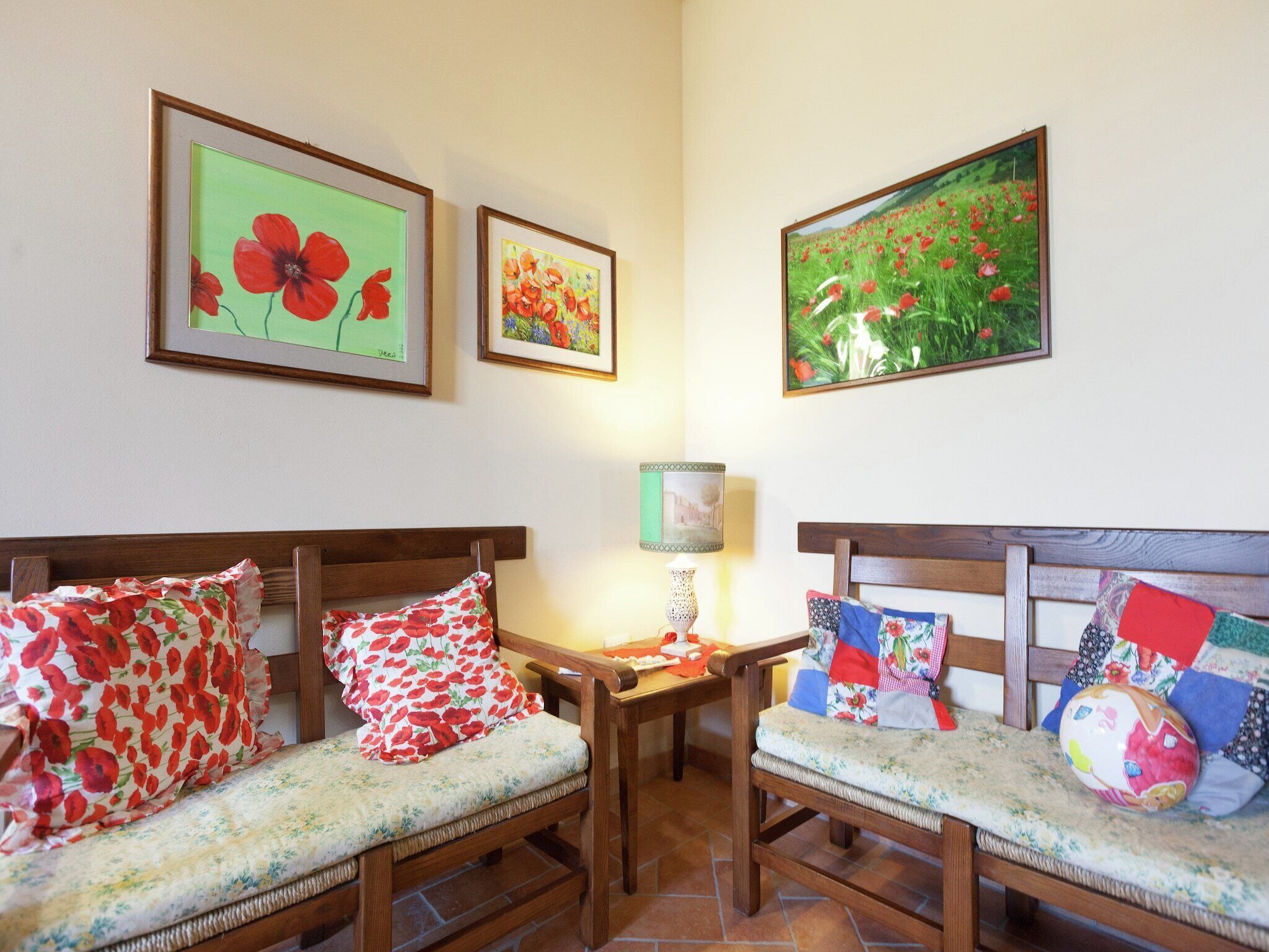 A cozy room with two wooden chairs and a small table, each with floral cushions. There are framed floral paintings on the wall.