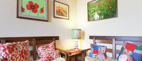 A cozy room with two wooden chairs and a small table, each with floral cushions. There are framed floral paintings on the wall.