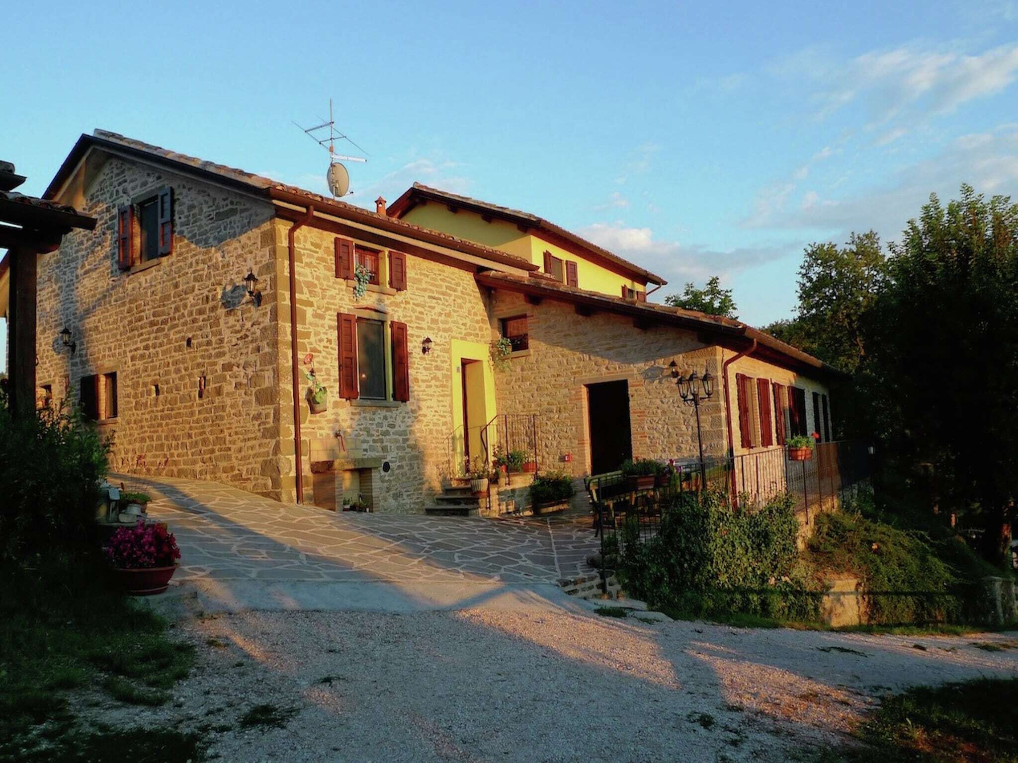Une maison en pierre avec un toit en pente, une antenne parabolique et une allée gravillonnée.