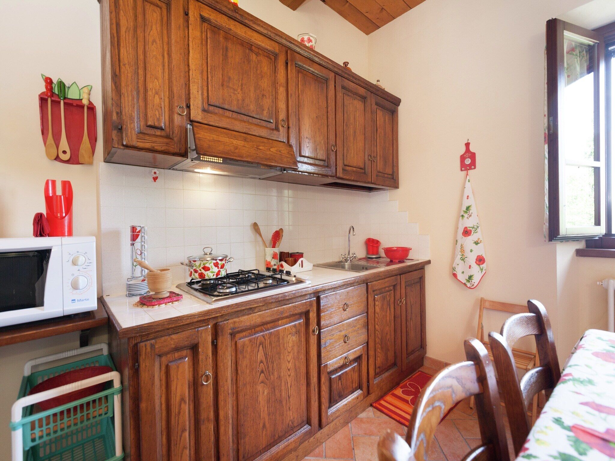 Une cuisine avec des meubles de rangement en bois, une cuisinière, un four à micro-ondes et une fenêtre.