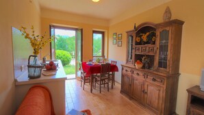 A dining area with a red tablecloth, wooden cabinets, and a view through a glass door to a garden. - Apartment in Marche with Pool and Privacy (Apecchio)