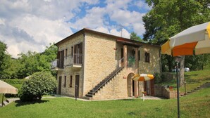 A stone building with a balcony, a staircase, and a grassy area with a picnic setup. - Apartment in Marche with Pool and Privacy (Apecchio)