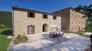 A stone building with a courtyard, a table with chairs, and a large umbrella. - Mansion in Apecchio near Lake (Apecchio)