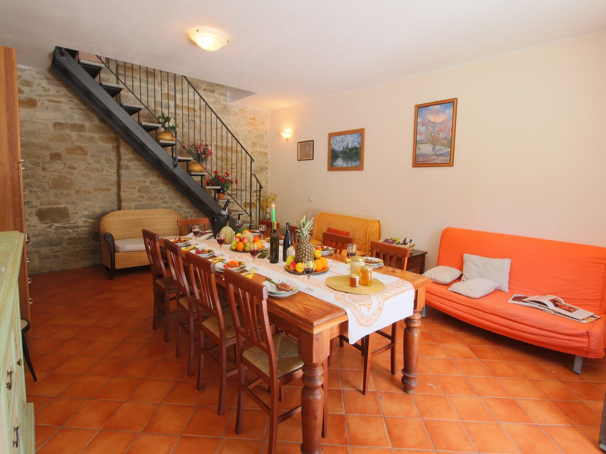 Un comedor con una mesa de madera dispuesta para cuatro personas, rodeada de sillas. Una escalera con barandilla de metal conduce a un nivel superior.