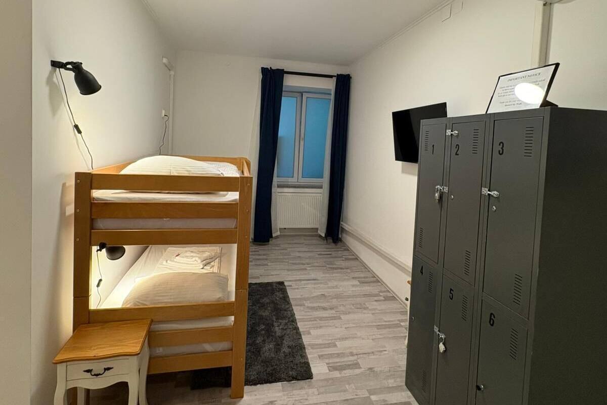 Ett sovrum med en våningssäng, ett skrivbord, en stol, en garderob och ett fönster med gardiner.