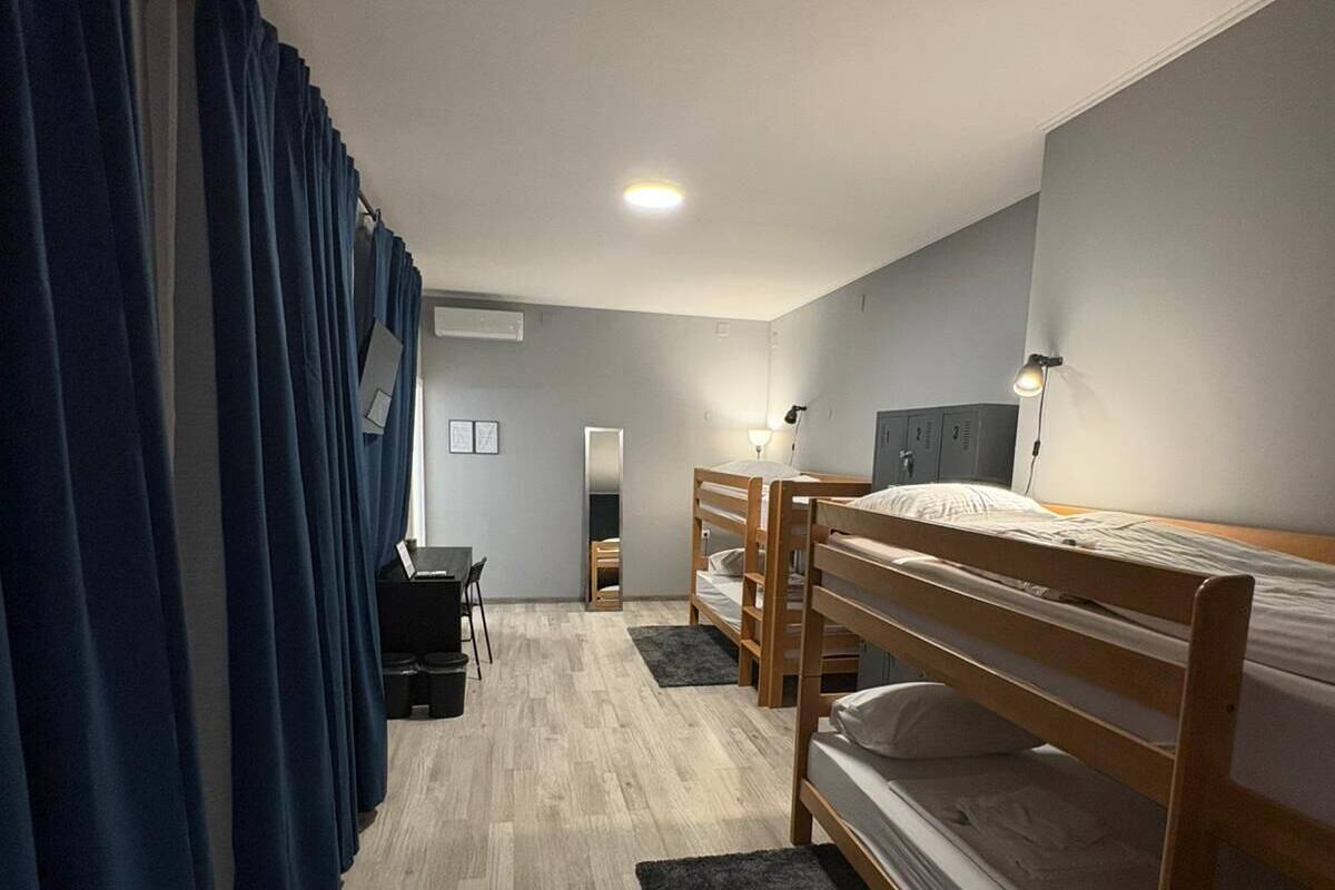 Ett studentrum med våningssängar, ett skrivbord, en stol, en spegel och en lampa.