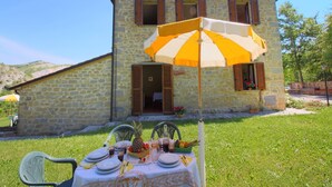A stone building with a table set for a meal outdoors, featuring a yellow umbrella. - Apartment in Marche with Pool Access (Apecchio)