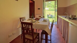 A dining area with a table set for two, a bottle of wine, and a view of a garden through an open door. - Apartment in Marche with Pool Access (Apecchio)