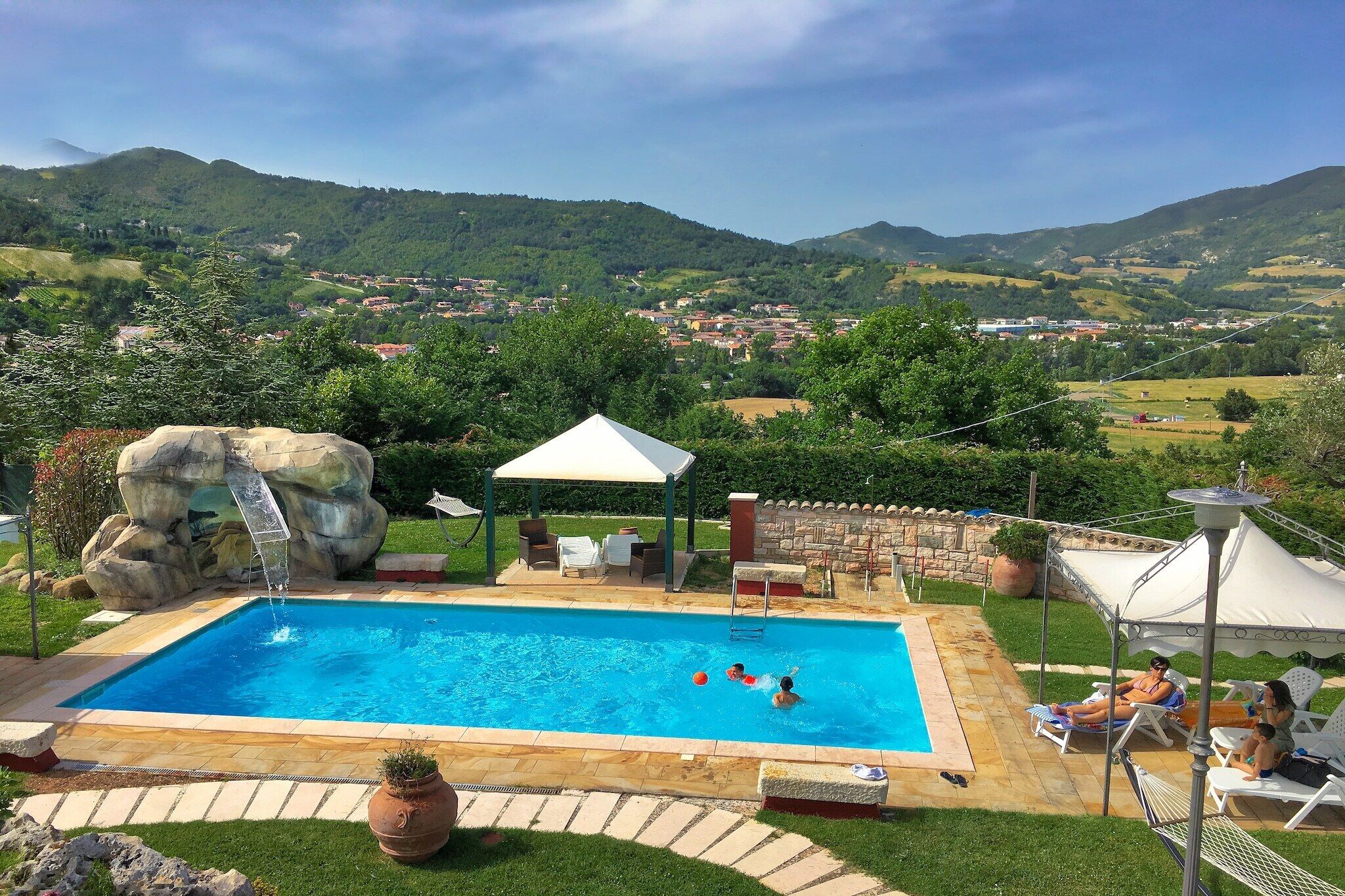 Una piscina con una formación rocosa, sillas de descanso y una cubierta blanca.