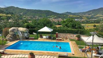 Una piscina con una formación rocosa, sillas de descanso y una cubierta blanca.
