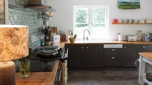 A modern kitchen with dark cabinets, a stove, and a window. - Stunning 3 bedroom Cottage on a private estate in SW Scotland (Mossdale)