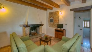 Un salon chaleureux avec une cheminée, des canapés verts, une table basse en bois et un mur en pierre.
