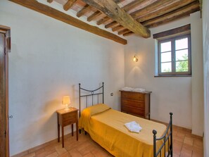 Een slaapkamer met een bed, nachtkastje, kapstok en een raam.