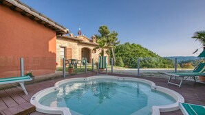 Une piscine avec une terrasse en bois, un espace patio doté de chaises, et une vue sur un bâtiment en pierre et des arbres.
