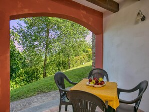 Een terras buiten met een tafel gedekt voor twee personen, een fruitschaal en uitzicht op een groen landschap.