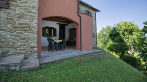 Un bâtiment en pierre avec une façade rouge, un patio couvert avec une table et des chaises, et une pelouse.