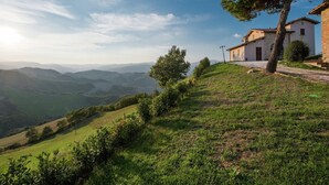 Un paysage rural avec des collines ondoyantes, une maison en pierre avec un toit de tuiles et un ciel dégagé.